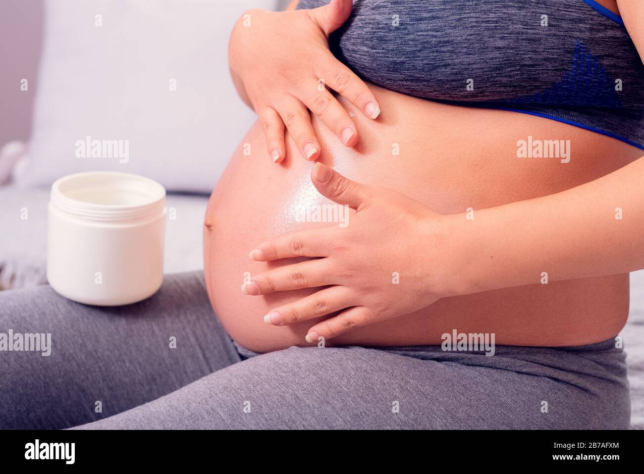 Pregnant woman rubbing her belly with body lotion against stretch marks