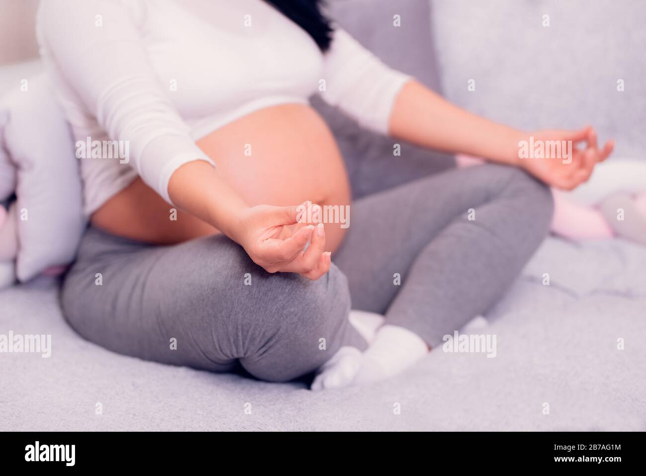 Pregnant woman sitting and relaxing in a lotus position while meditating and exposing her large belly. Stock Photo