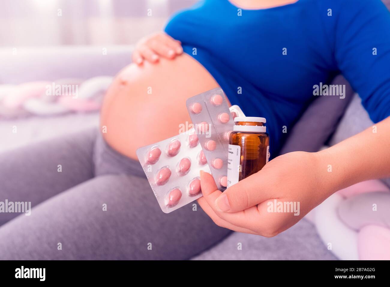 Vitamins during pregnancy. Pregnant woman holding pills in her hand and exposing her belly. Stock Photo
