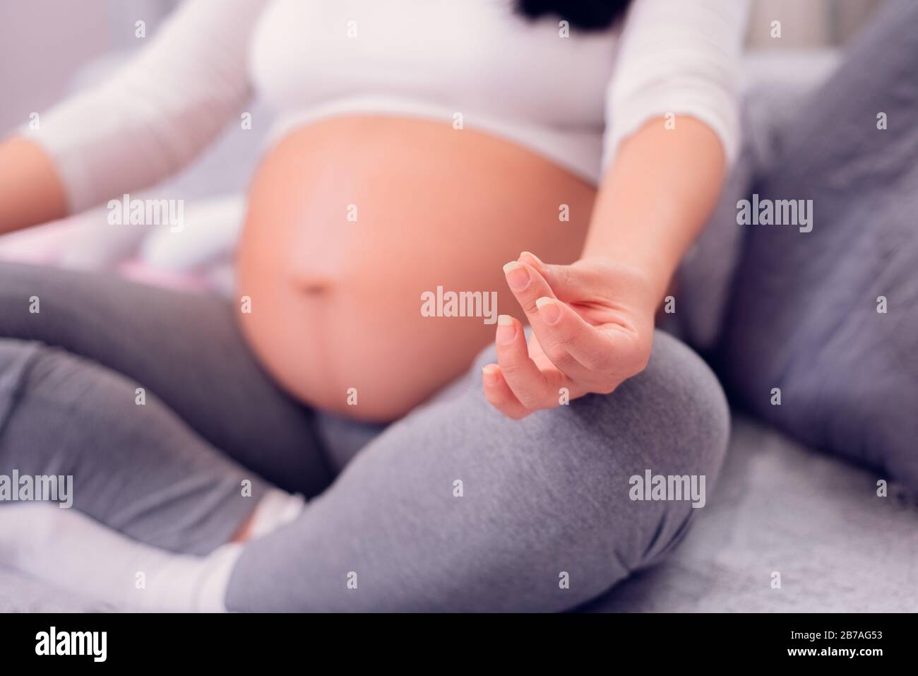 Pregnant woman sitting and relaxing in a lotus position while meditating and exposing her large belly. Stock Photo