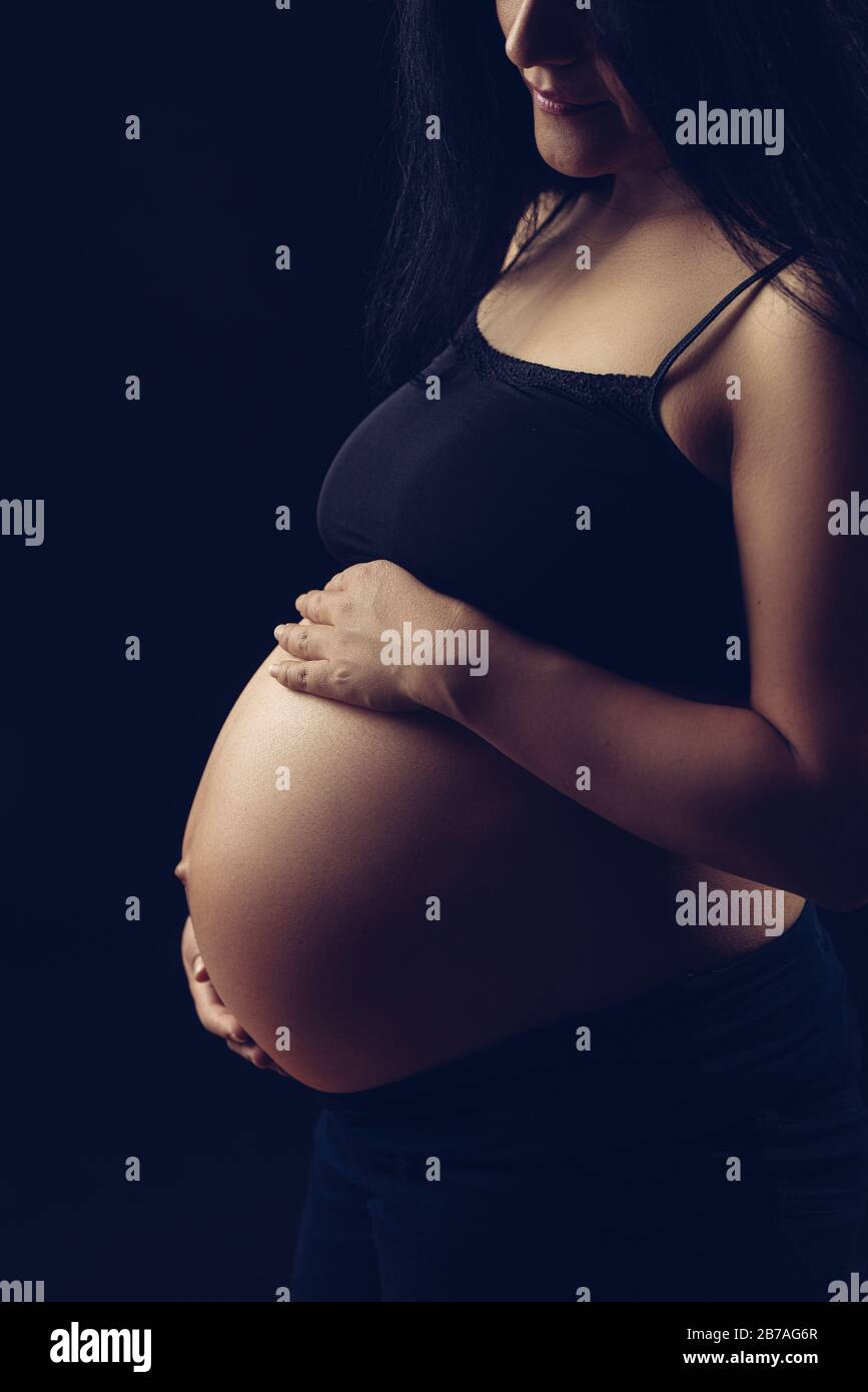 Subtle light revealing pregnant woman, holding belly with two hands. Stock Photo