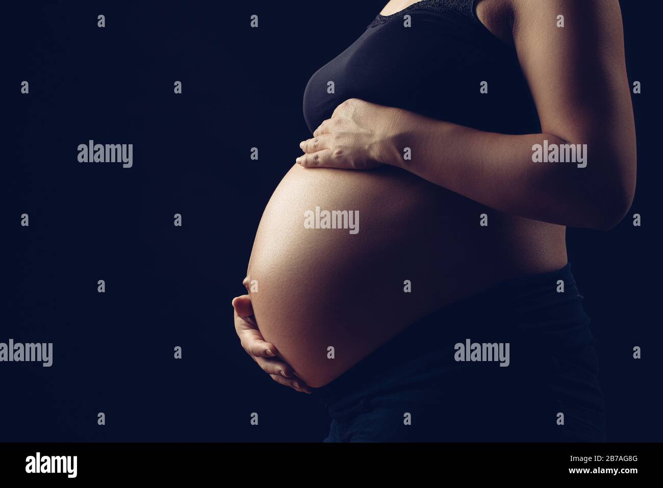 Subtle light revealing pregnant woman, holding belly with two hands Stock Photo Alamy