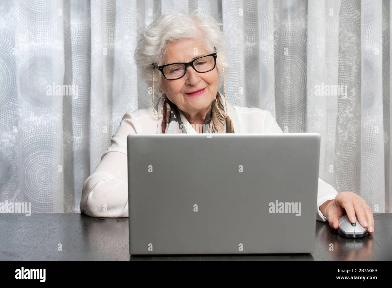 old lady with glasses looking at a computer on a wooden table. concept of technology , grandma, health Stock Photo