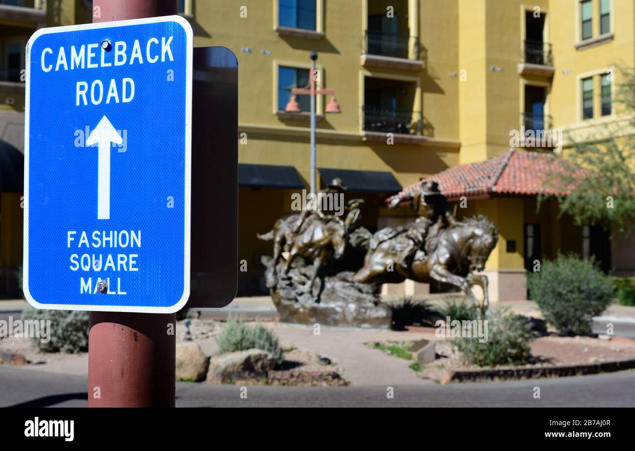 A blue and white traffic sign with directions to Camelback Road and Fashion Square Mall with the Hashknife Pony Express sculpture in Scottsdale, AZ Stock Photo