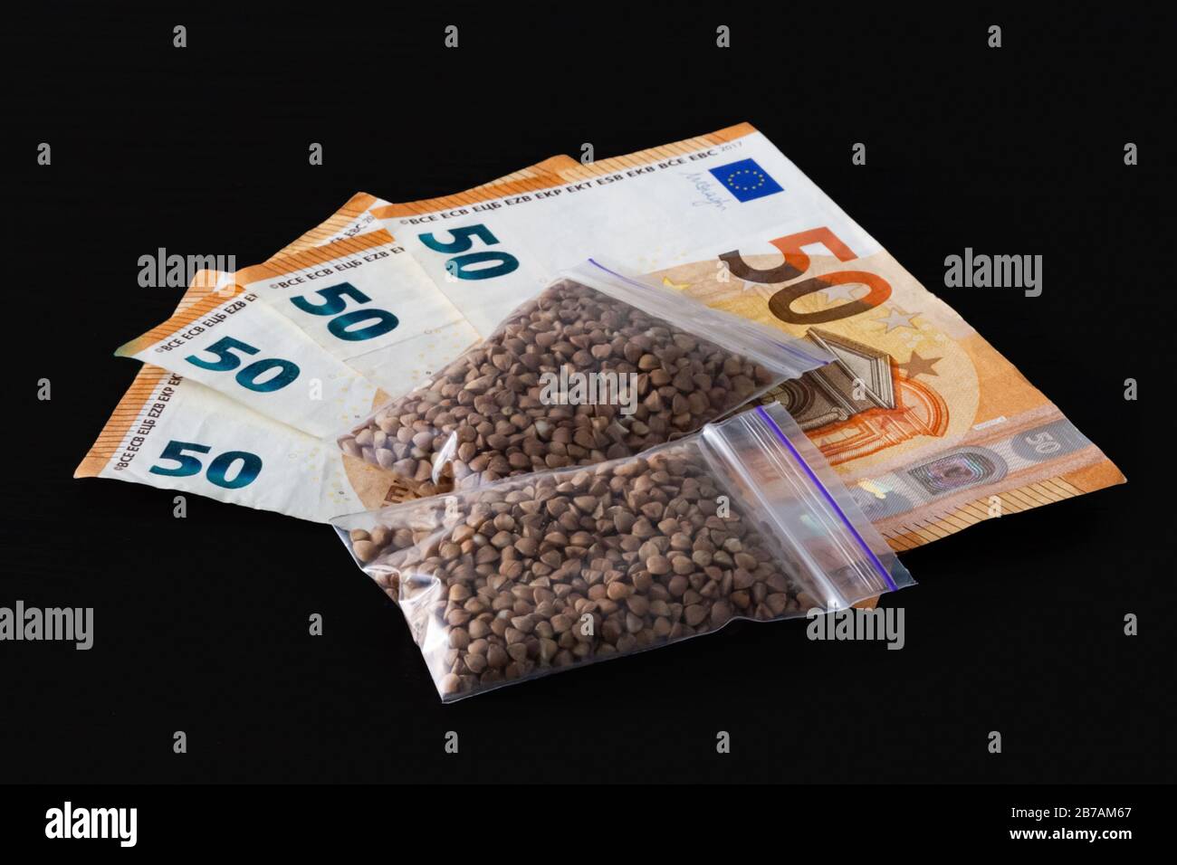 Raw buckwheat groats in small transparent plastic bags, small dose, expensive, a lot of euro money. on black background. Stock Photo
