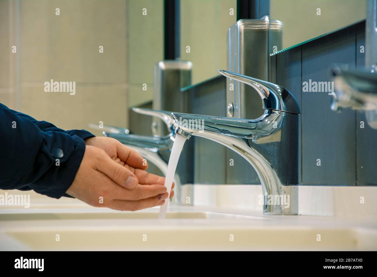 Unrecognizable man is washing his hands in the public toilet Stock Photo