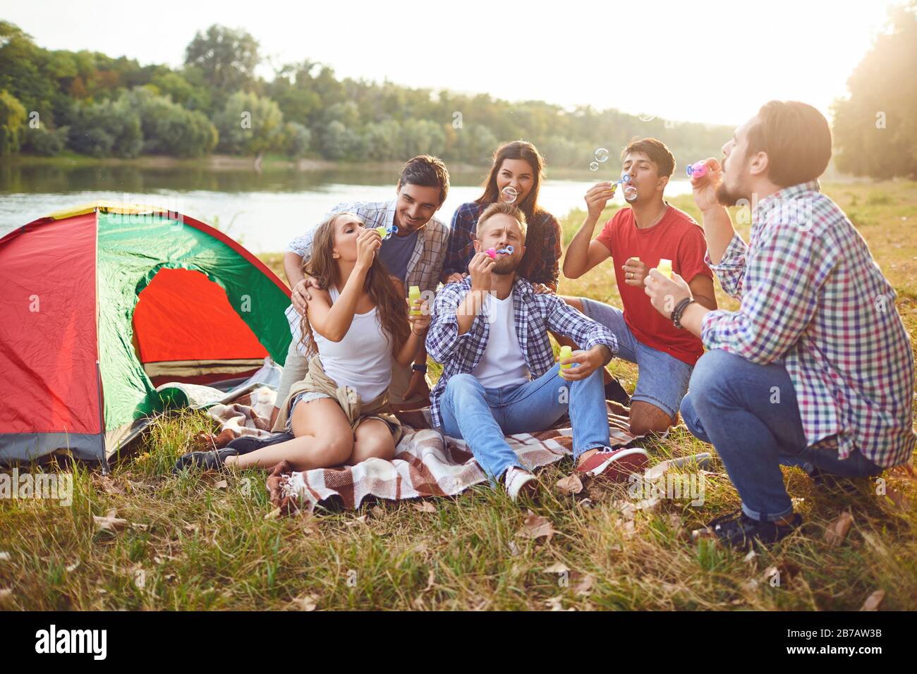 Young people make soap bubbles while sitting on the grass on in nature. Stock Photo