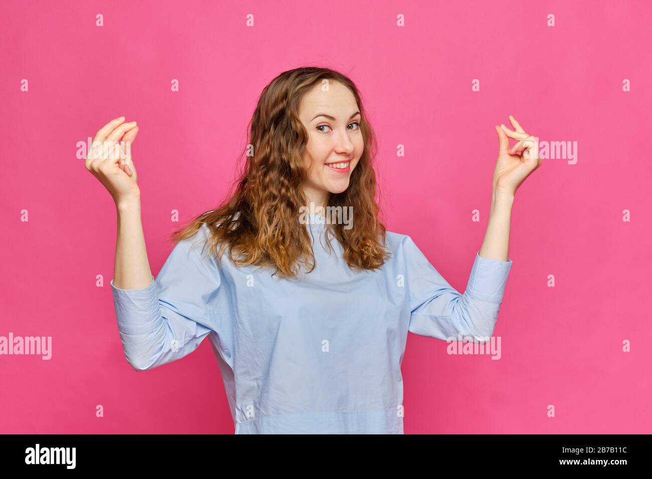 Stylish caucasian girl in a pale blue t-shirt shows a gesture of snapping fingers on a pink background. Close up. Stock Photo