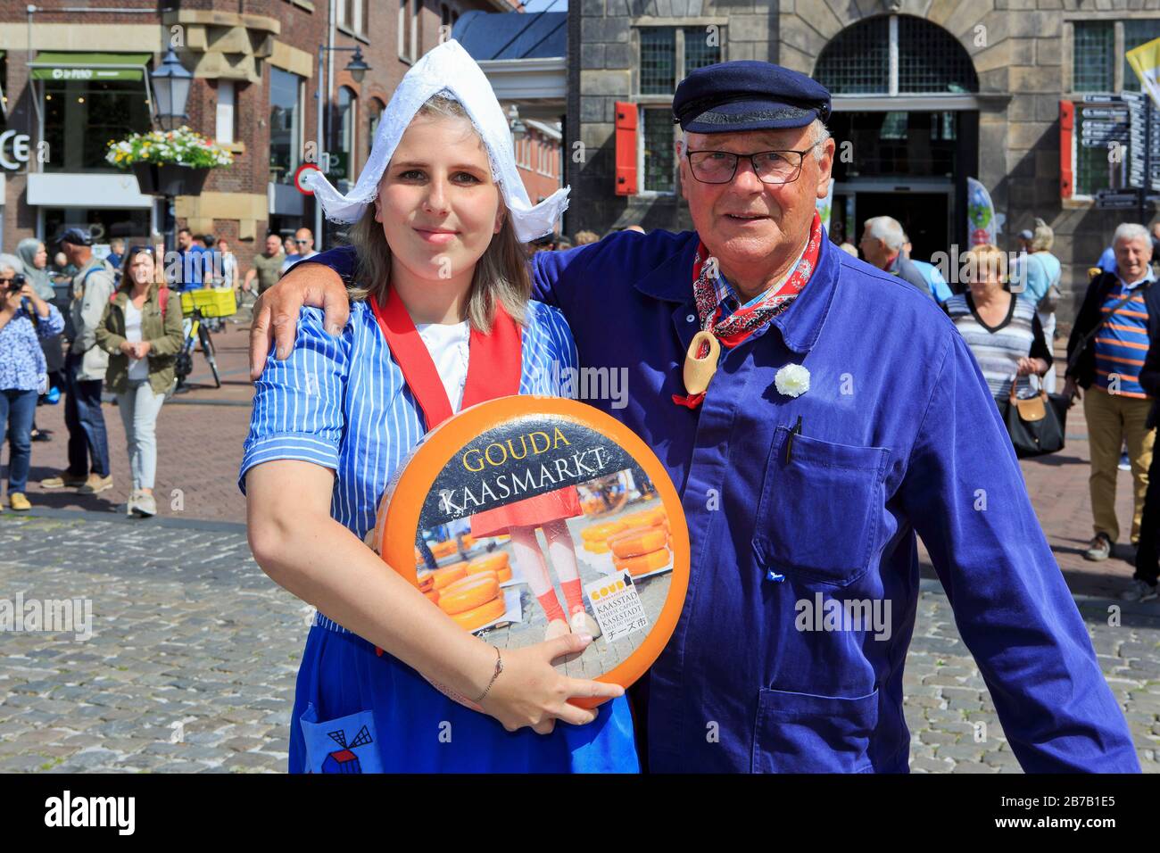 Girl in traditional Dutch attire holding a Gouda cheese ball and a cheese farmer at the Cheese Market in Gouda (South Holland), Netherlands Stock Photo