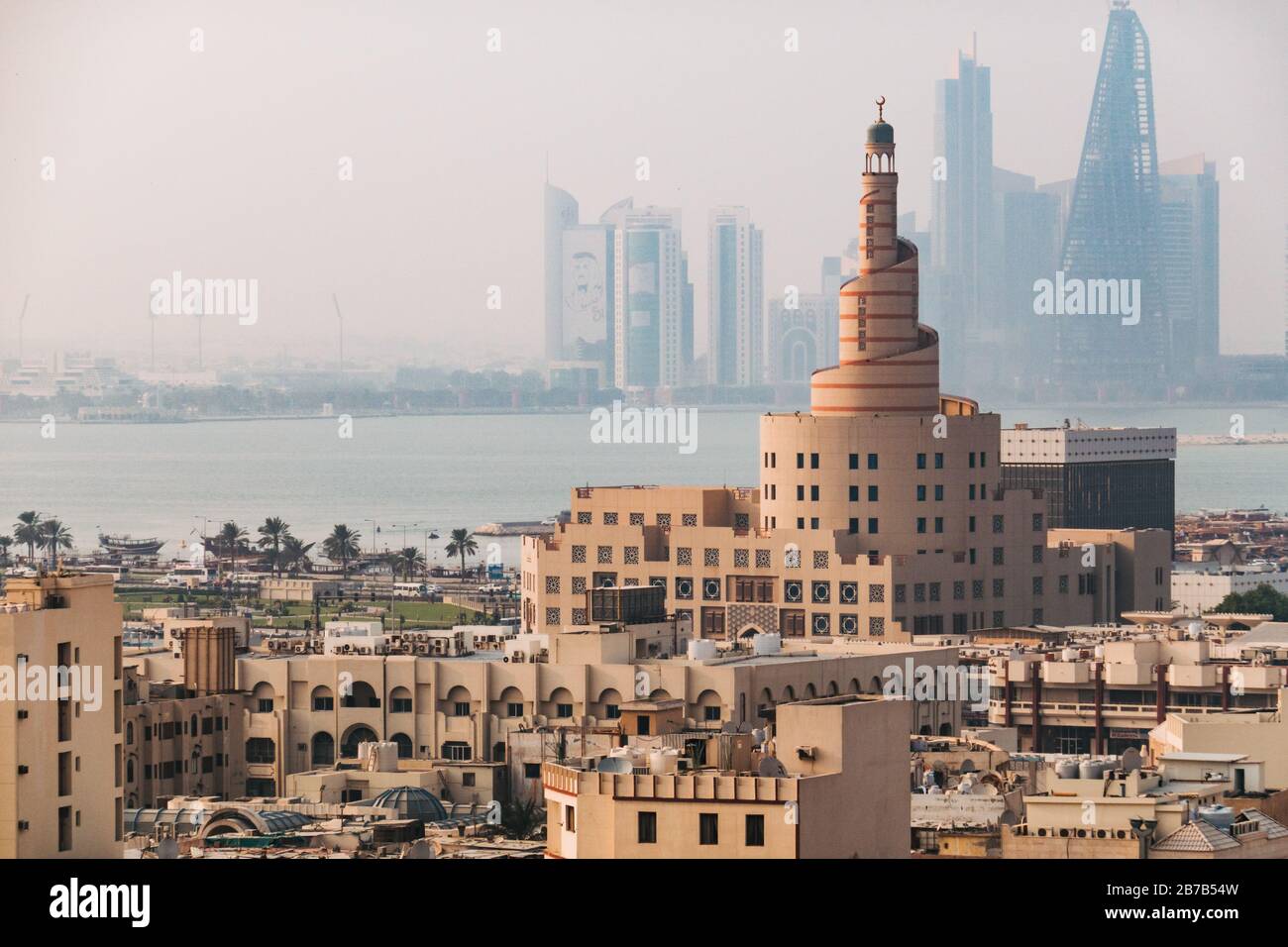 The famous spiral mosque of the Kassem Darwish Fakhroo Islamic Centre near Souq Waqif in Doha, Qatar. The city skyline can be seen behind in the haze Stock Photo