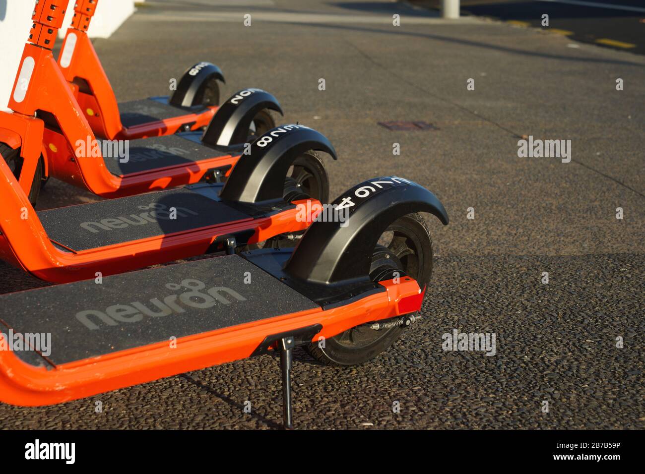 Four orange and black Neuron rent to ride electric scooters on a