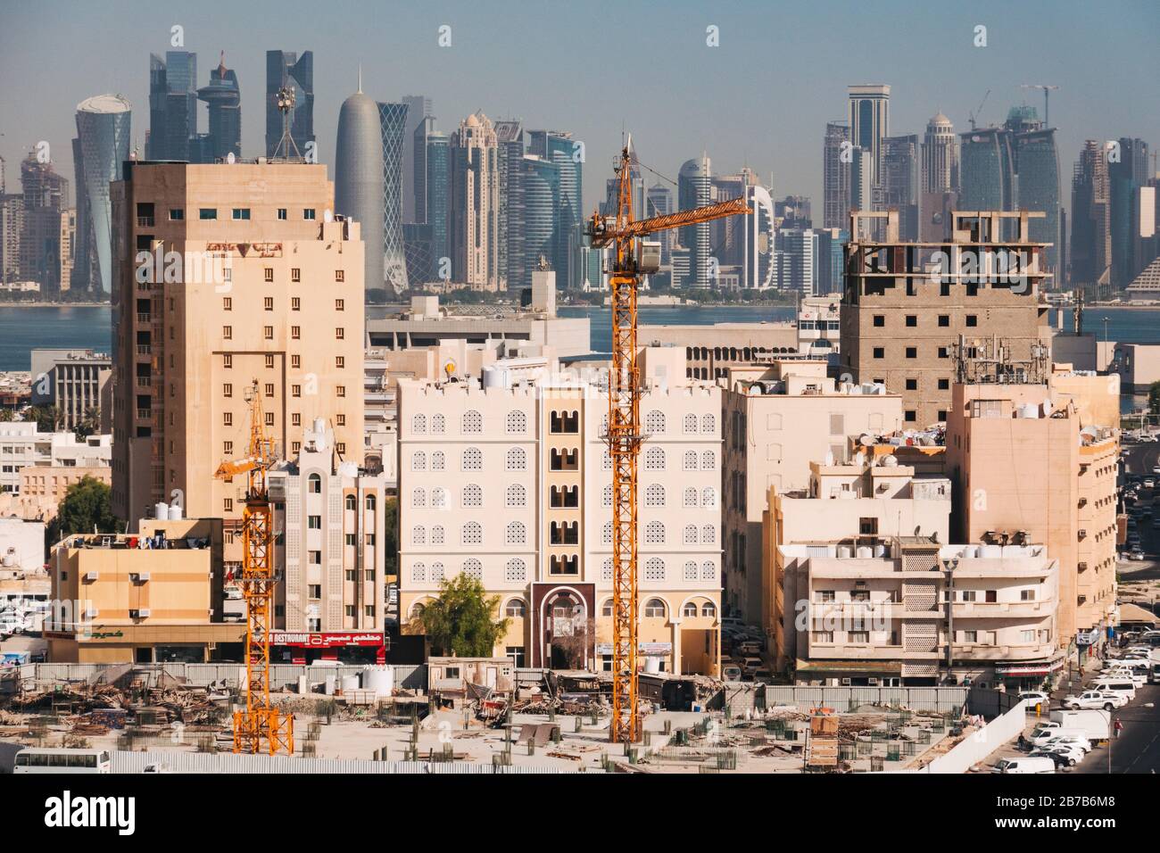 A crane and buildings under construction in Doha's Al Souq area, with the modern financial district skyline visible across the bay in the background Stock Photo