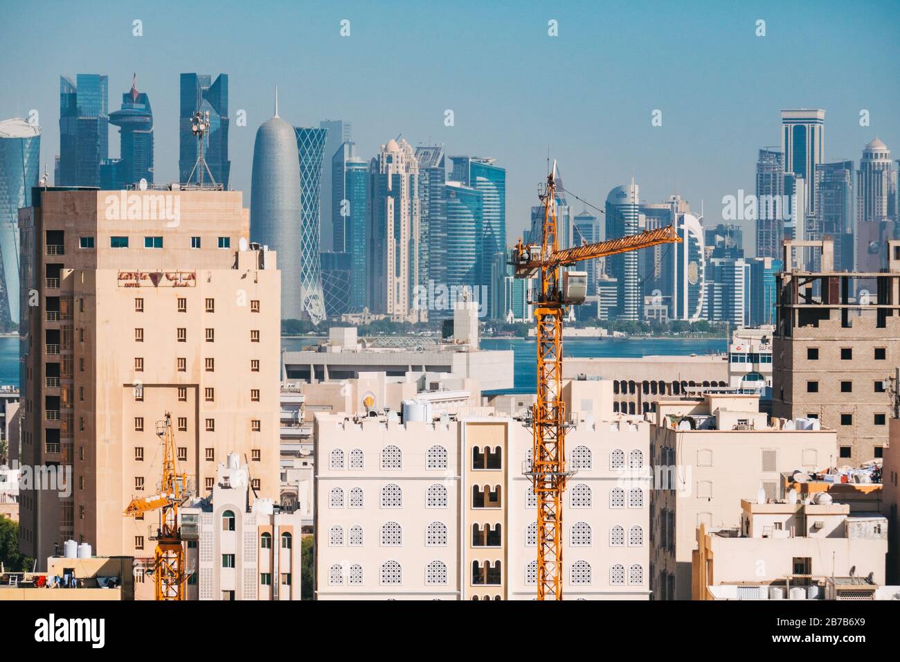 A crane and buildings under construction in Doha's Al Souq area, with the modern financial district skyline visible across the bay in the background Stock Photo