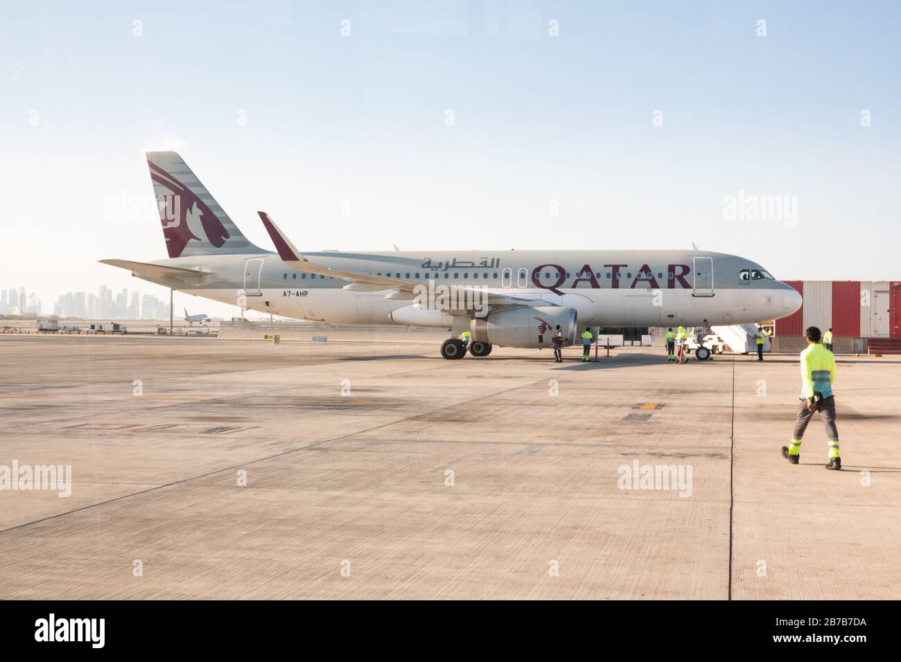 Ground crews attend a Qatar Airways Airbus A320 as it parks on a remote stand at Hamad International Airport, Doha Stock Photo