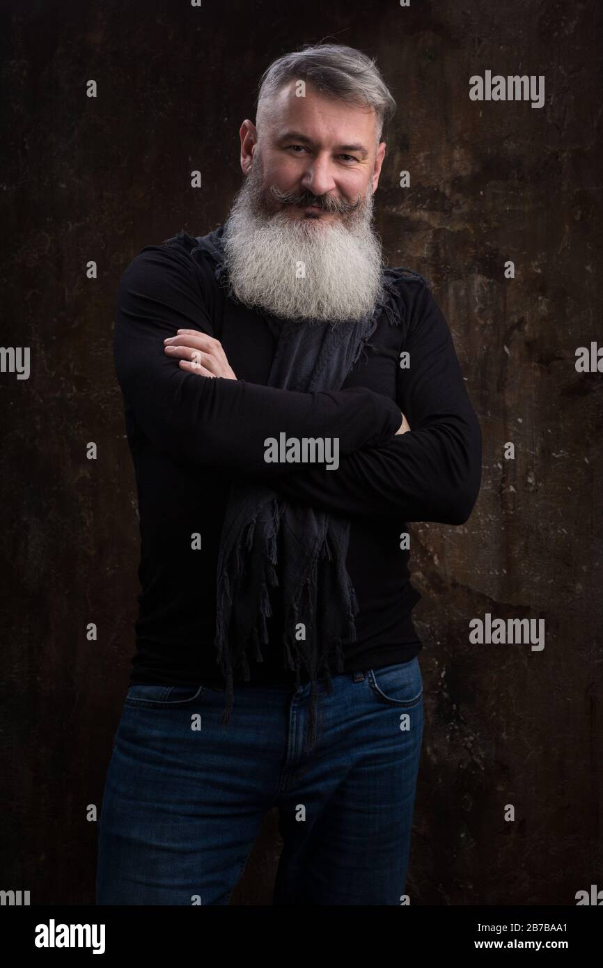 Studio portrait of handsome mature gray-haired bearded man against the dark wall, selective focus Stock Photo
