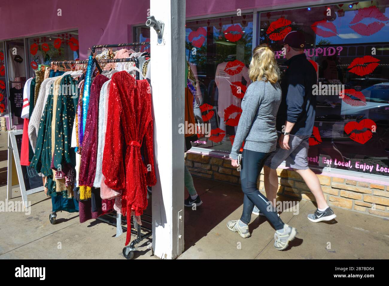 People wearing athletic clothing walking on sidewalk in front of storefronts with sparkly dresses on rack outside in old town Scottsdale, AZ, USA Stock Photo