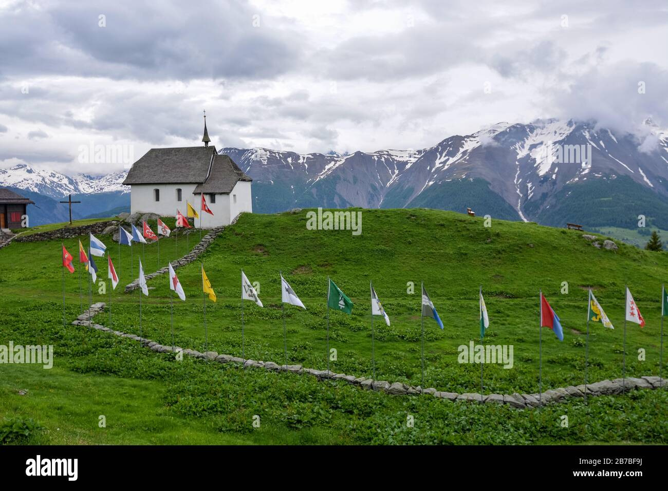 A church with lots of flags in the Swiss village Bettmeralp on a cloudy day Stock Photo