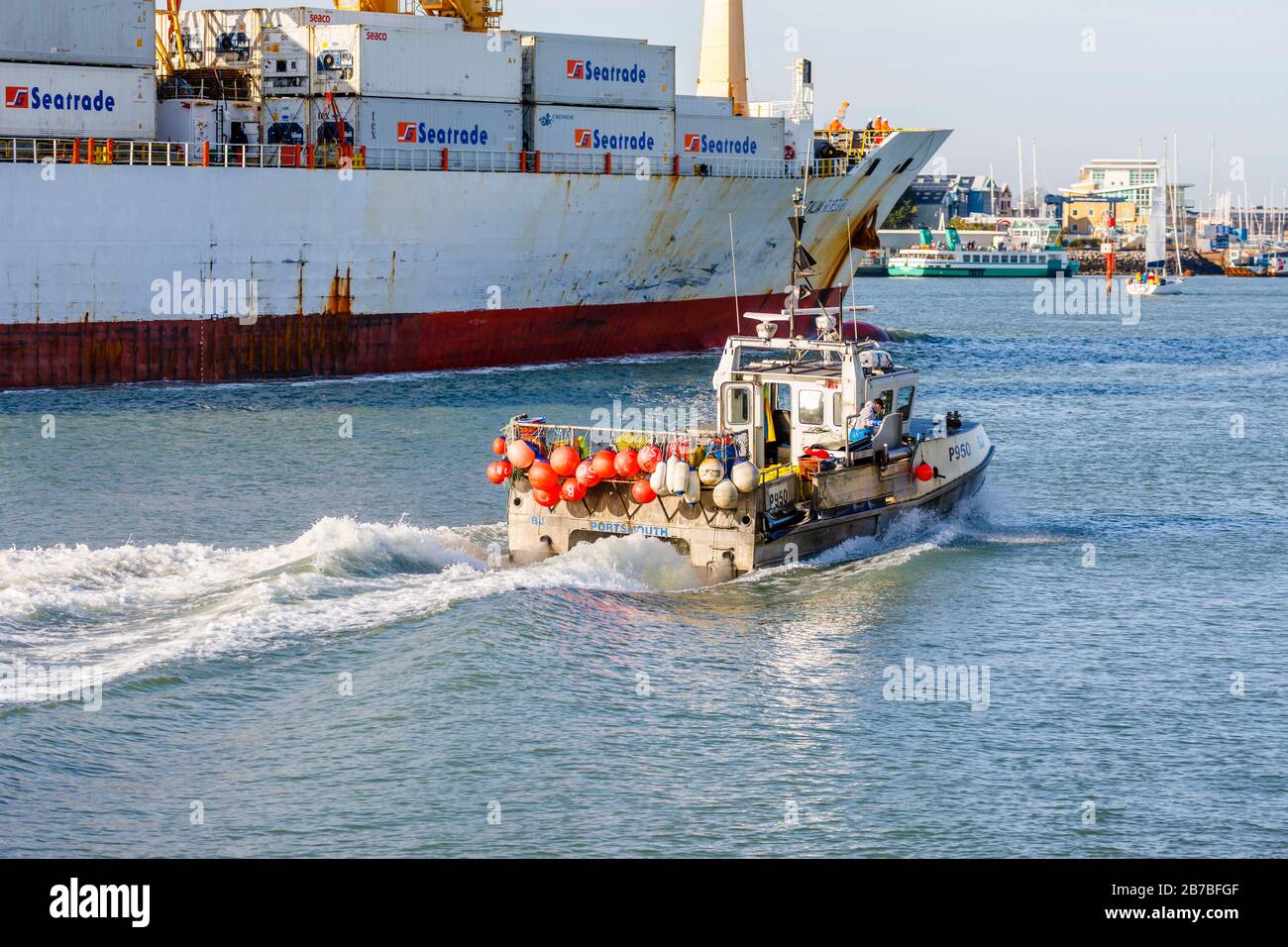 A small traditional fishing boat is dwarfed passing by a large container ship near Gosport in Portsmouth Harbour, Portsmouth, Hampshire, south England Stock Photo