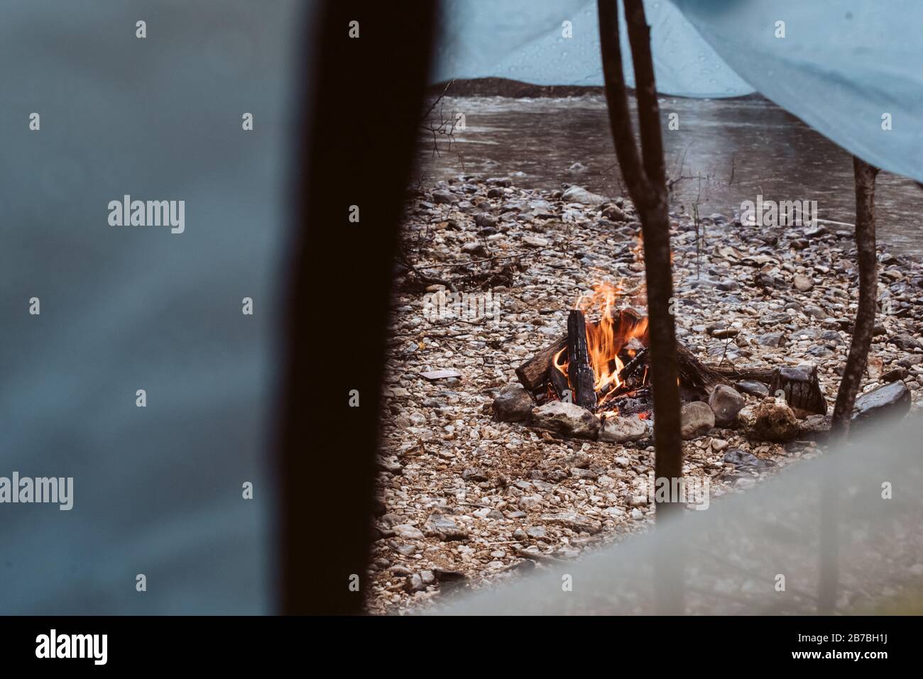 Fire burning in fire pit next to tent and river on camping trip Stock