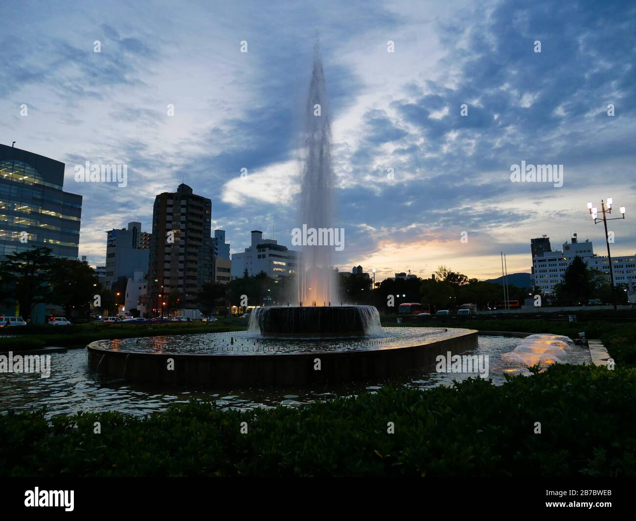 Illuminated fountain in Japanese park at night, cloudy filled sky in background sets the mood Stock Photo