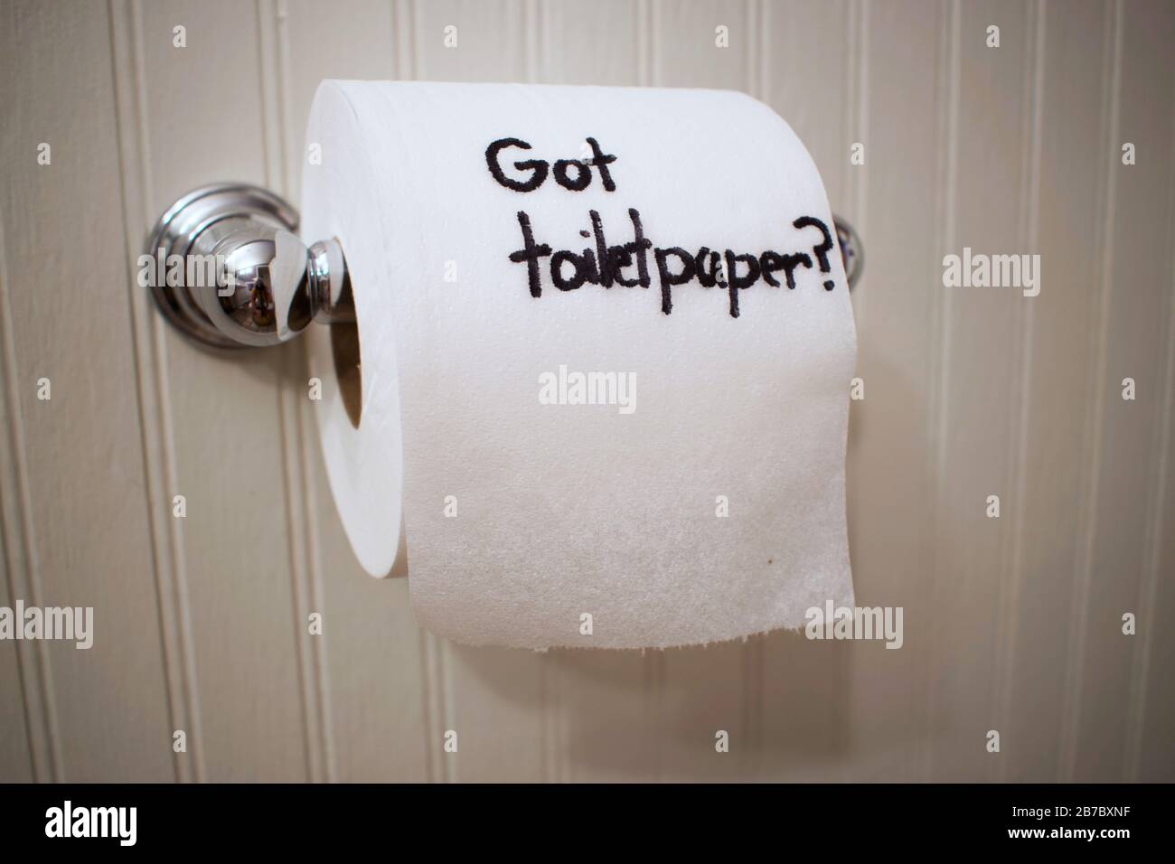 'Got Toilet Paper?' written on toilet paper roll with sharpie as it hangs on the wall on a silver spool. Stock Photo