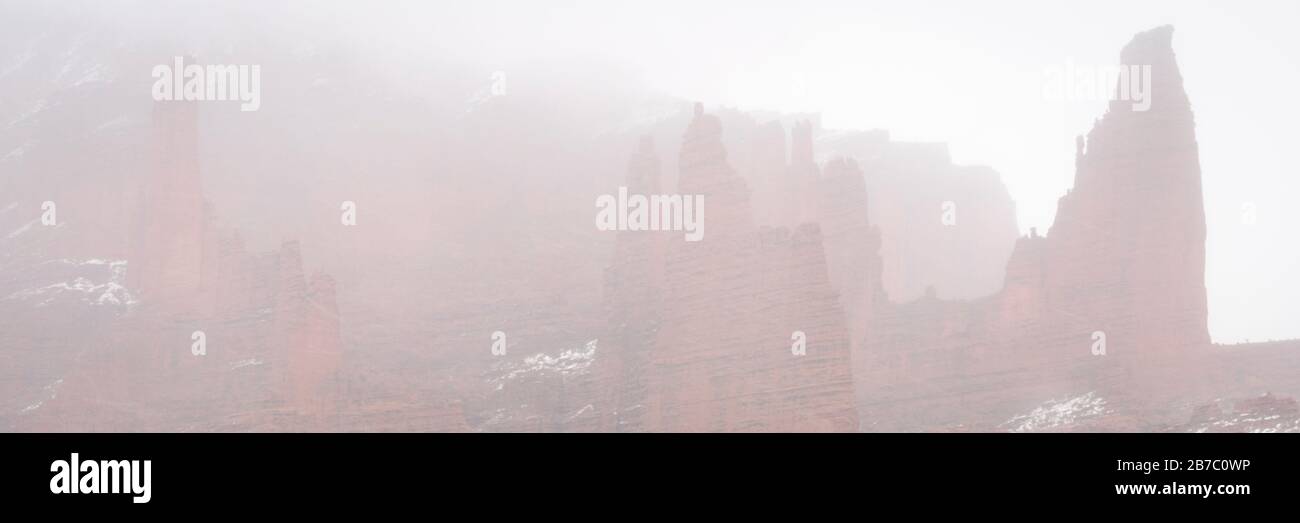 winter scenery of southwest landscape with falling snow and fog - panorama of Fisher Towers in the Moab area in Utah Stock Photo