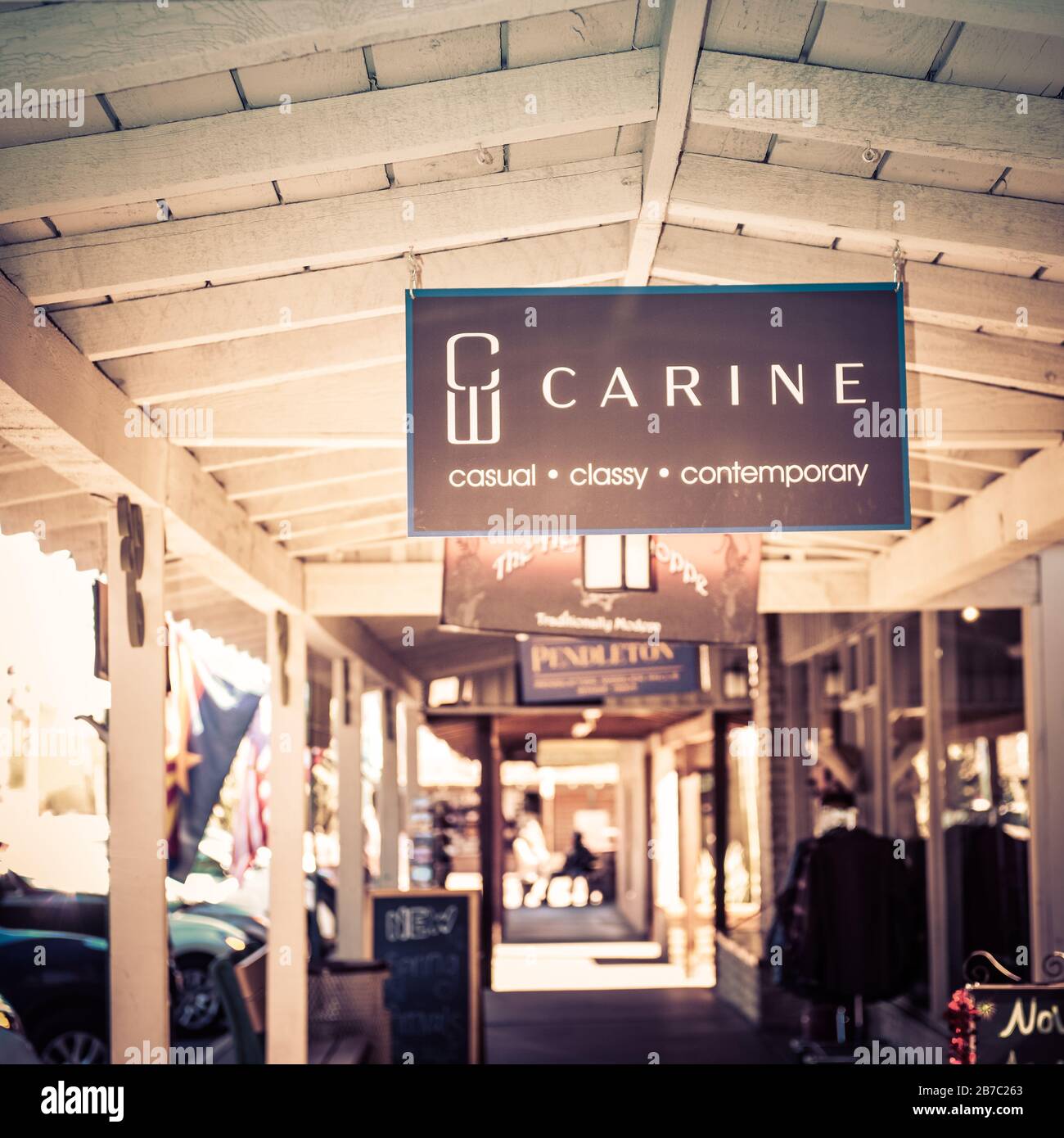 An overhead sign for Carine W, a fashionable boutique, hangs from the old wooden ceiling of the portal along the sidewalk and storefronts in old town Stock Photo