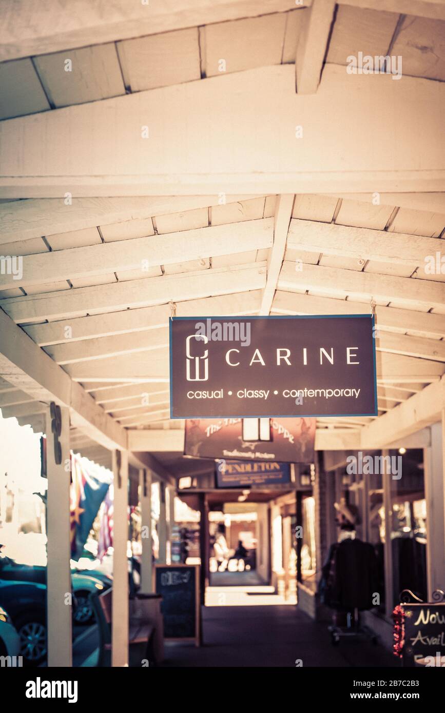 An overhead sign for Carine W, a fashionable boutique, hangs from the old wooden ceiling of the portal along the sidewalk and storefronts in old town Stock Photo
