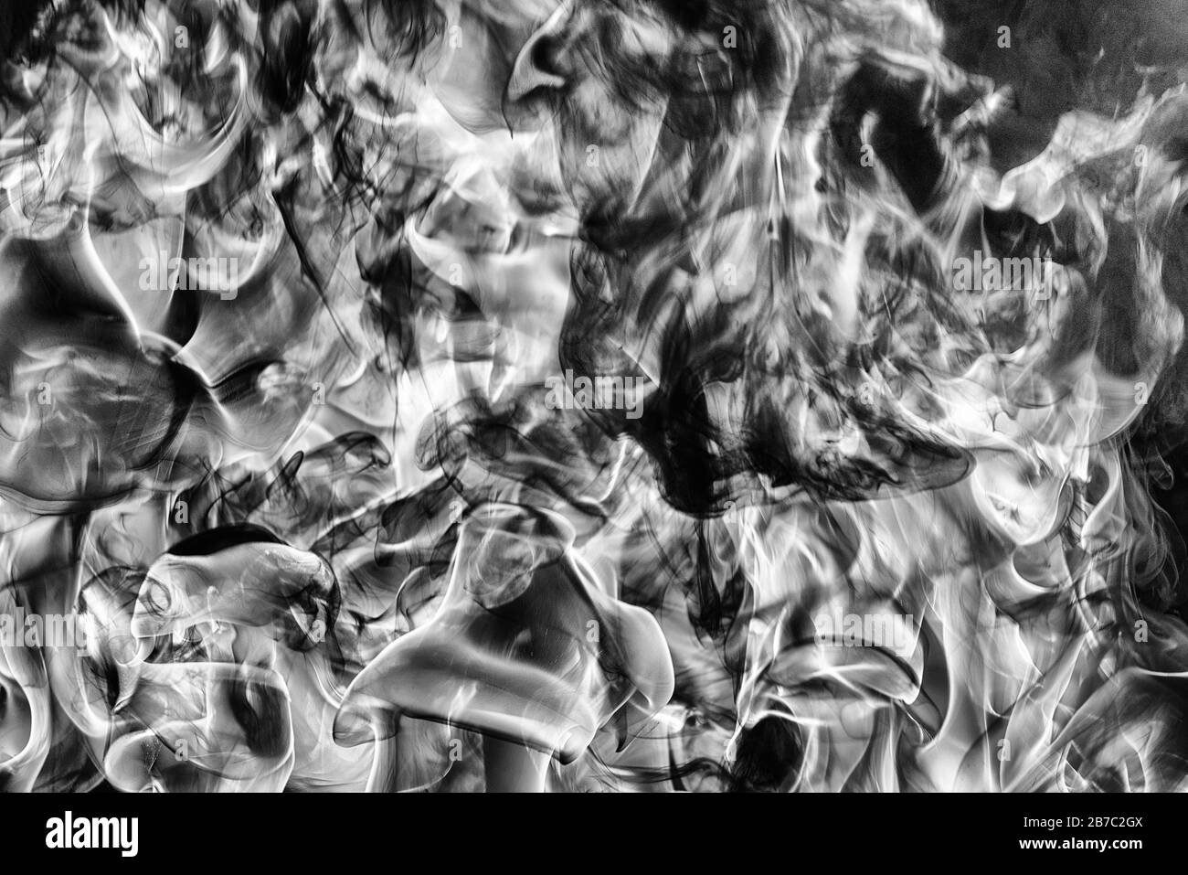 Abstract clouds of natural black smoke and white huge flame of strong fire. Dangerous firestorm abstract background. Monochrome photography Stock Photo