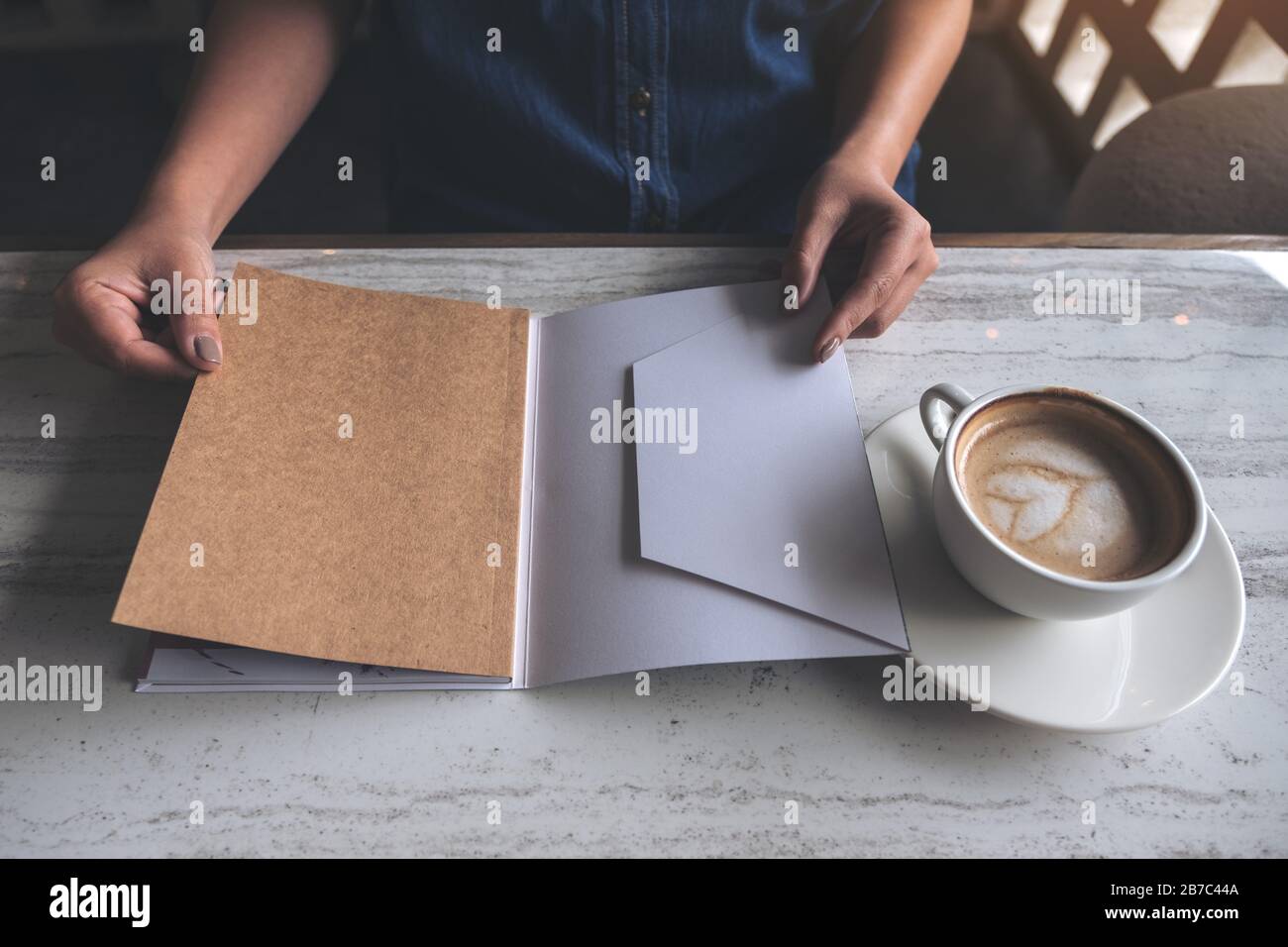 Closeup image of a woman opening a book with coffee cup on table in modern cafe Stock Photo