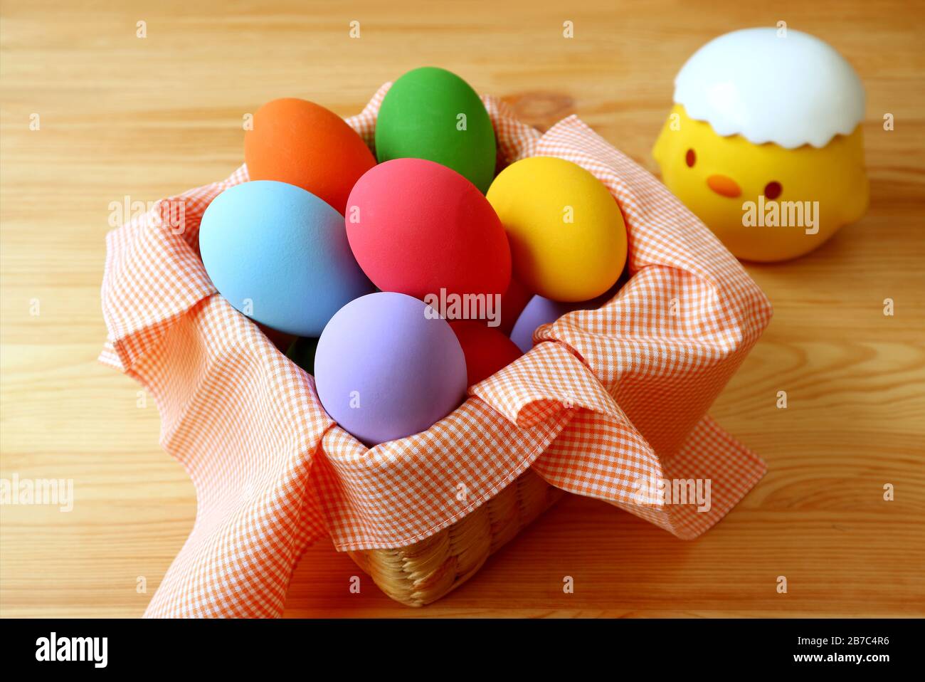 Basket of Multi-color Easter Eggs with a Cute Chick Sugar Pot on Wooden Table Stock Photo