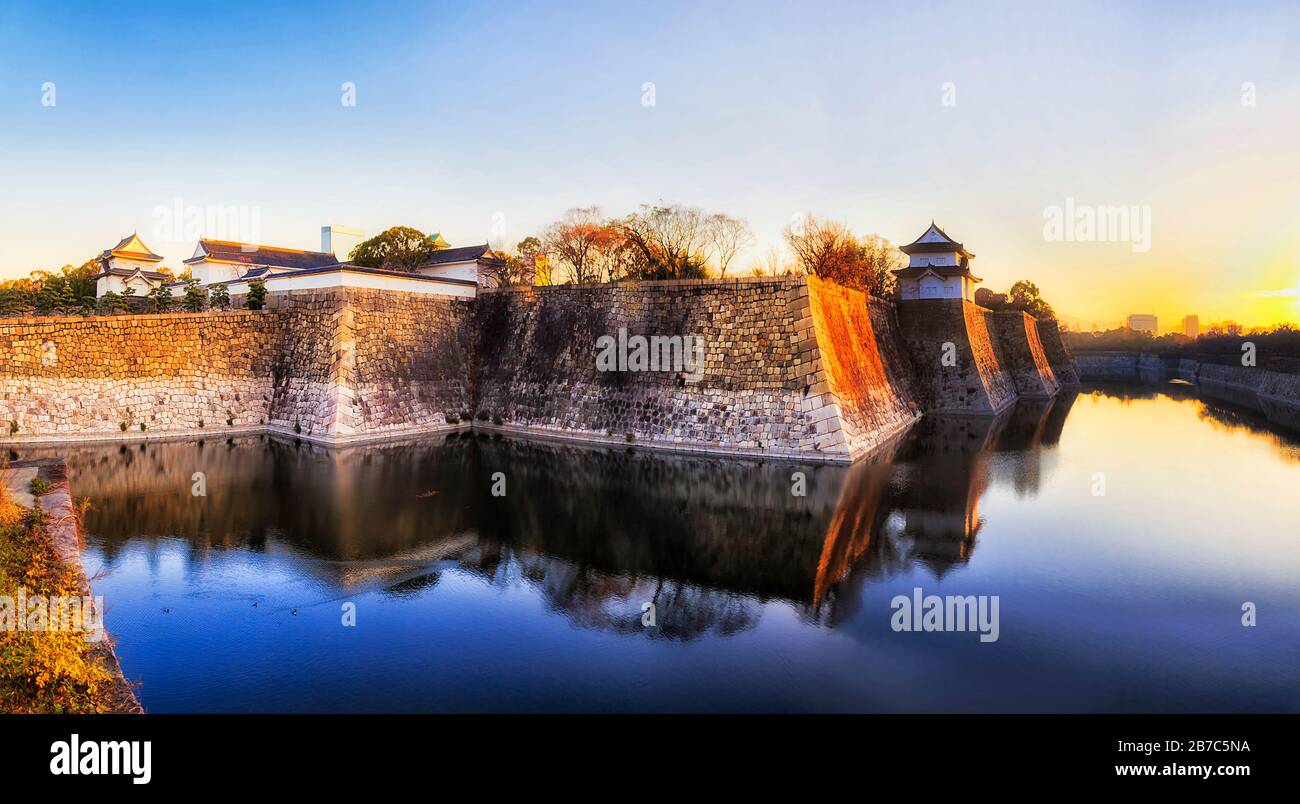 Water moat around stone walls of historic palace, park and castle in Osaka city of Japan. Soft rising sun over horizon. Stock Photo