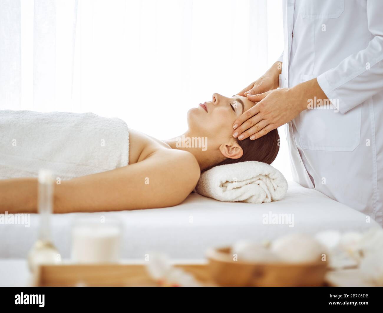 Beautiful brunette woman enjoying facial massage with closed eyes. Relaxing treatment in medicine and spa center concepts Stock Photo
