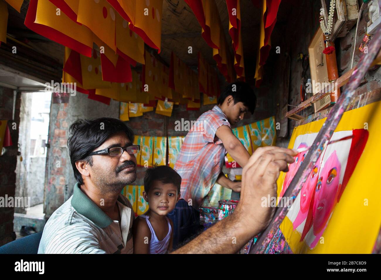 Proshanto Kumar Das, son of Raj Kumar Das, best known as RK Das, one of the first generation rickshaw artists in Bangladesh, is engaged in painting a rickshaw art while his on Joy helps him at his studio in capital Dhaka, on May 3, 2012. The rickshaw art is a form of pop art that depicts our urban culture and folklore of Bangladesh. Rickshaws were first introduced in Bangladesh in the 1930s from Japan, where the three-wheeled vehicles were known as 'nintaku'. The idea of decorating the leg-powered contraptions took off in Bangladesh the 1950s with the tradition following the simple yet colourf Stock Photo