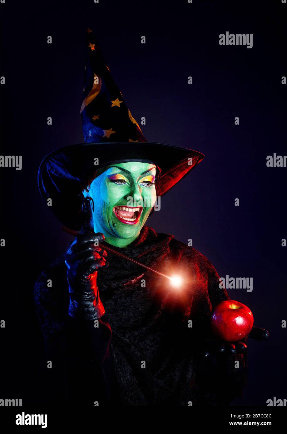 Witch with green skin holding glowing wand and conjure red apple at ...