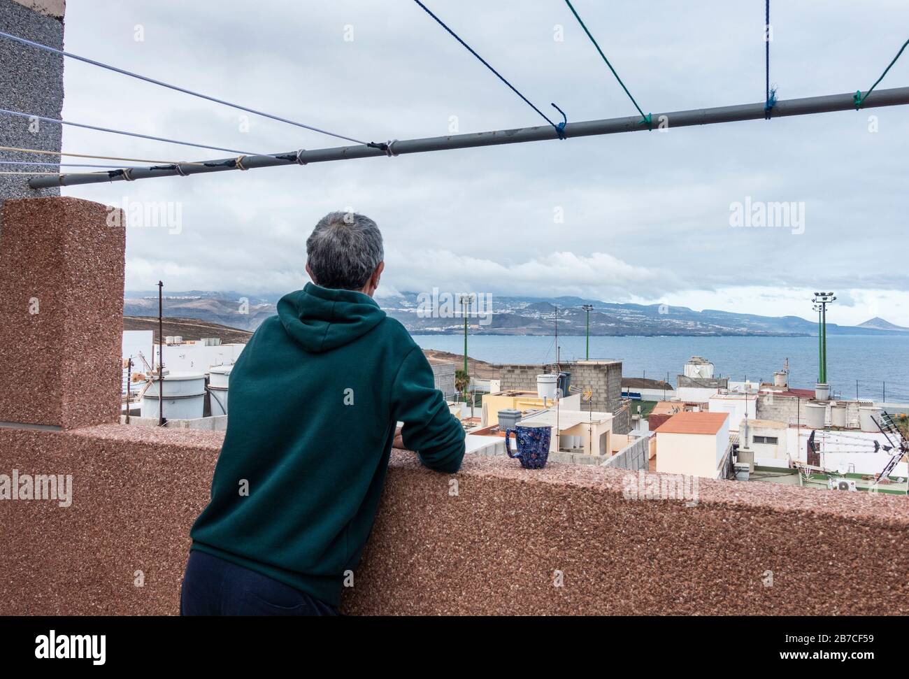 Las Palmas, Gran Canaria, Canary Islands, Spain. 15th March 2020. A local resident takes his morning coffee from rooftop balcony in Las Palmas on Gran Canaria as Spain goes into lockdown mode to combat Coronavirus. A state of emergecy has been declared in Spain, with the whole population ordered to stay indoors. People will be allowed to go to work (if unable to work from home), attend essential medical appointments and shop for essential items.  Credit: Alan Dawson/Alamy Live News Stock Photo