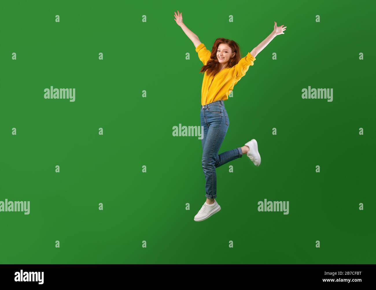 Joyful Girl Jumping With Raised Hands Over Green Studio Background ...
