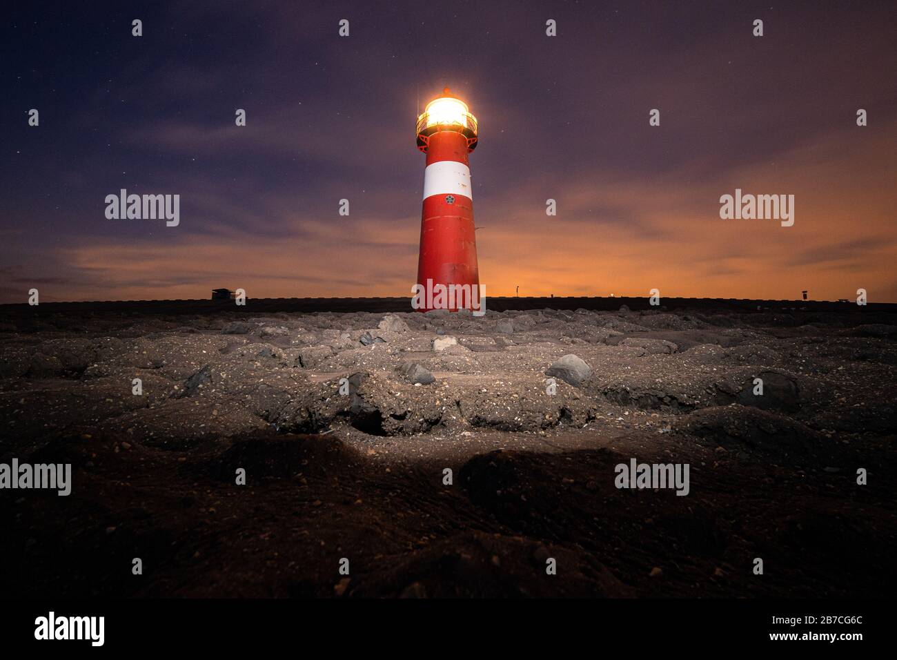 Low angle shot of a red and white lit lighthouse on a sandy beach under ...