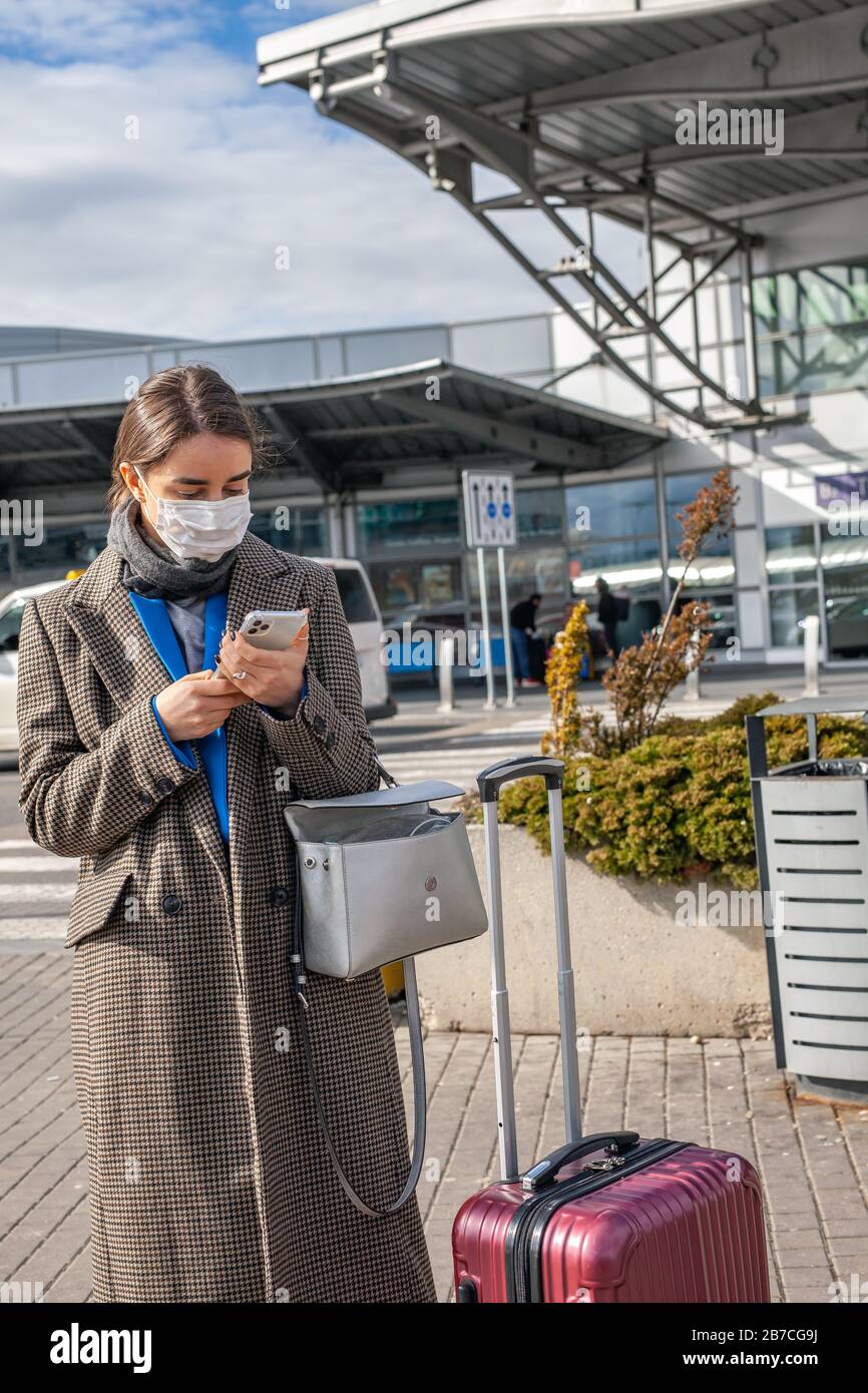 Woman wearing a face mask with her smartphone in hands outside an airport Stock Photo