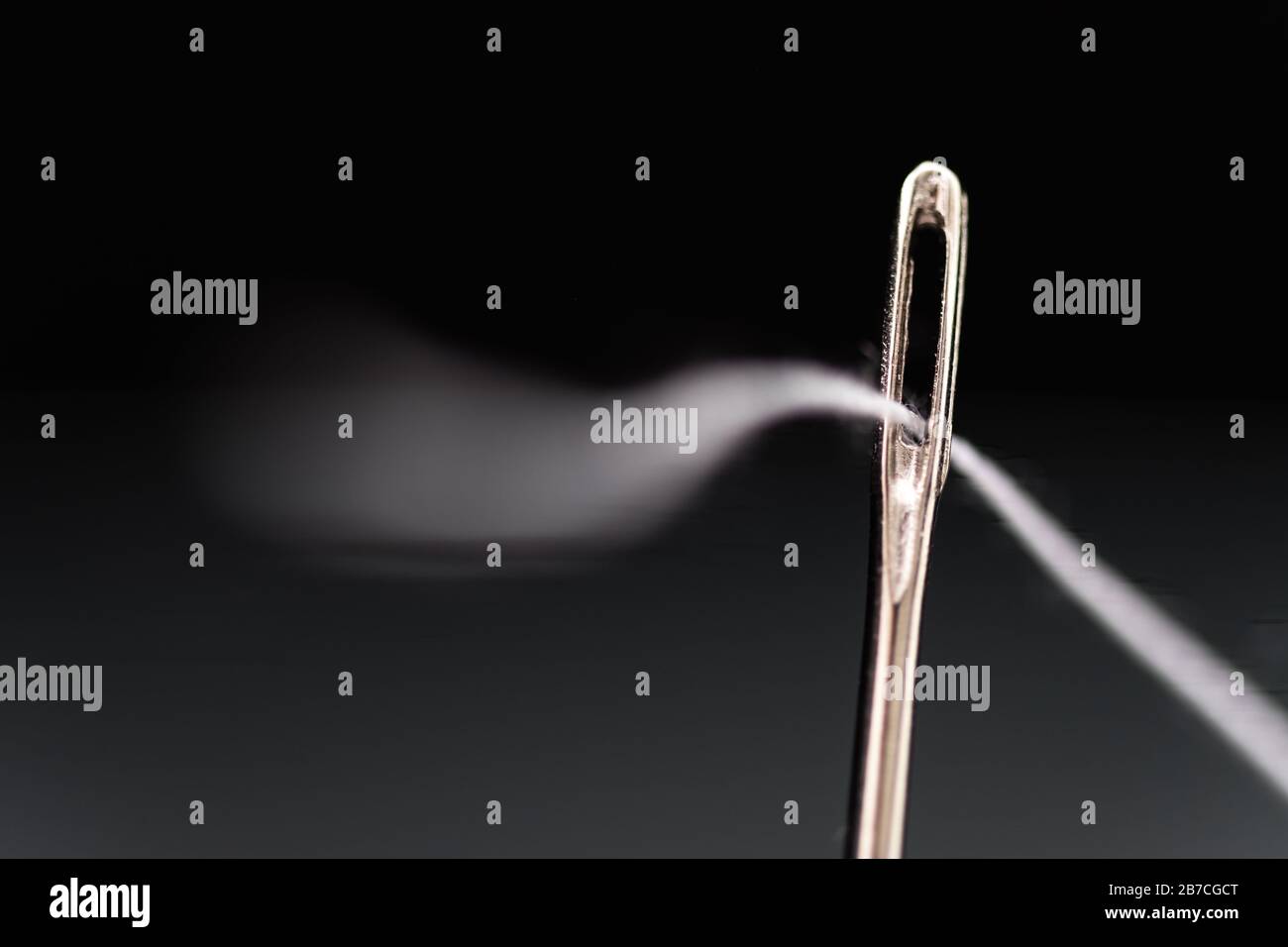 Needle with white thread threaded on black background Stock Photo