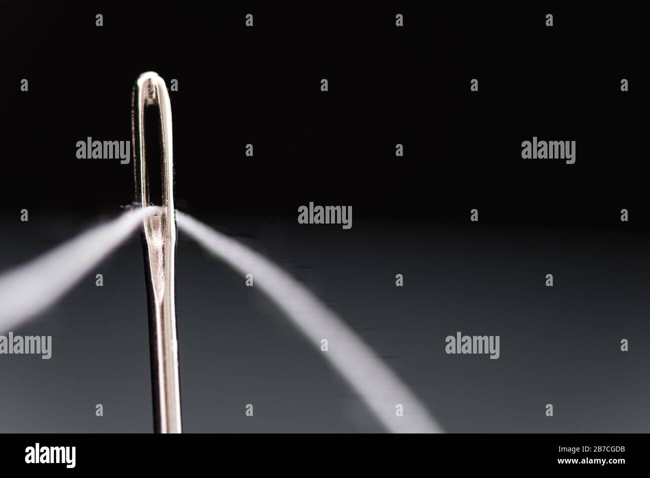 Needle with white thread threaded on black background Stock Photo