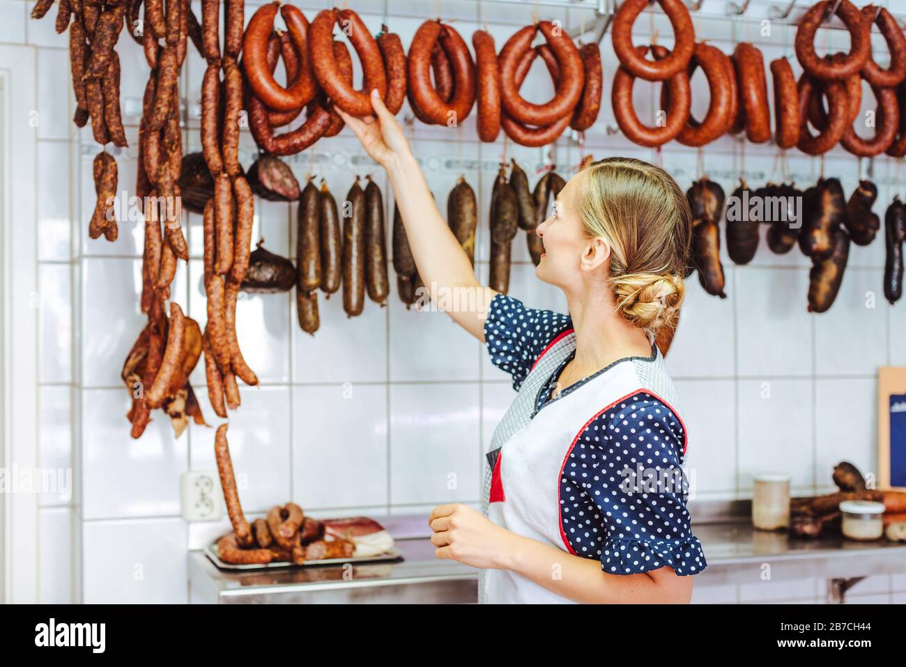 Saleslady getting sausages from the hook in butchery shop Stock Photo