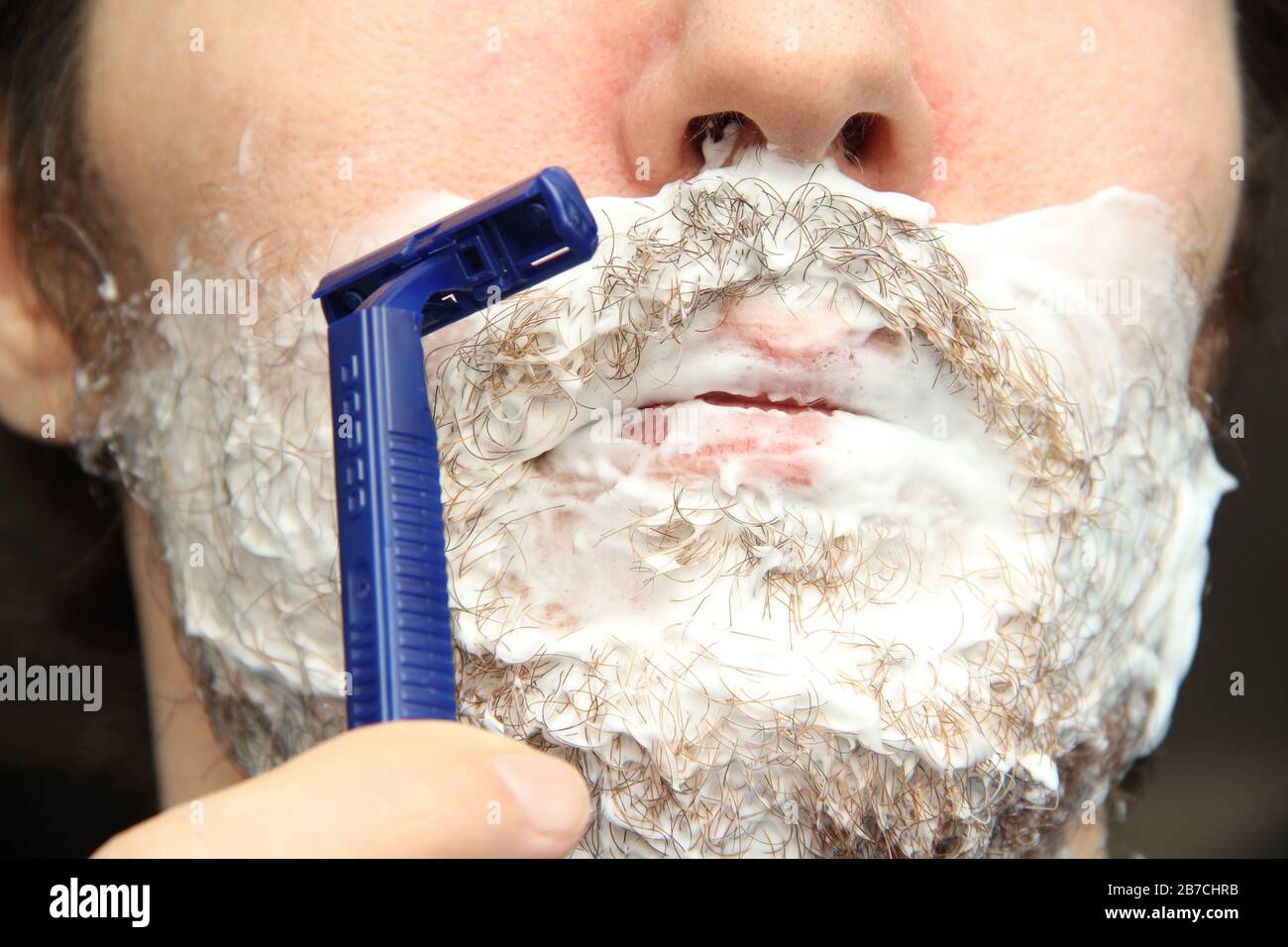 A man shaves his beard with a blue disposable safety razor. White