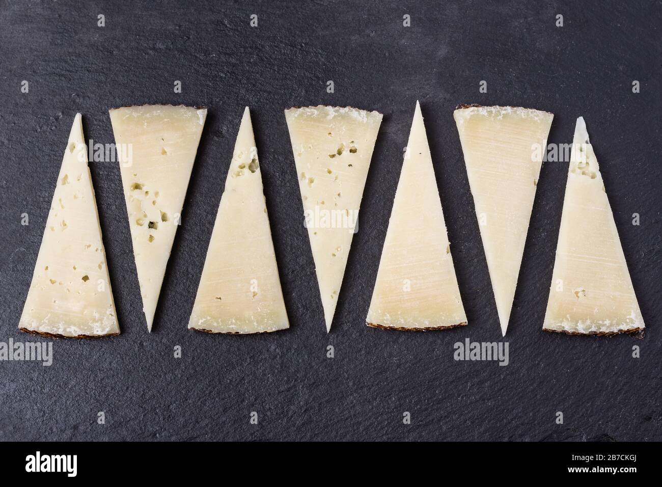 Triangleshaped slices of aged spanish manchego cheese on a dark stone