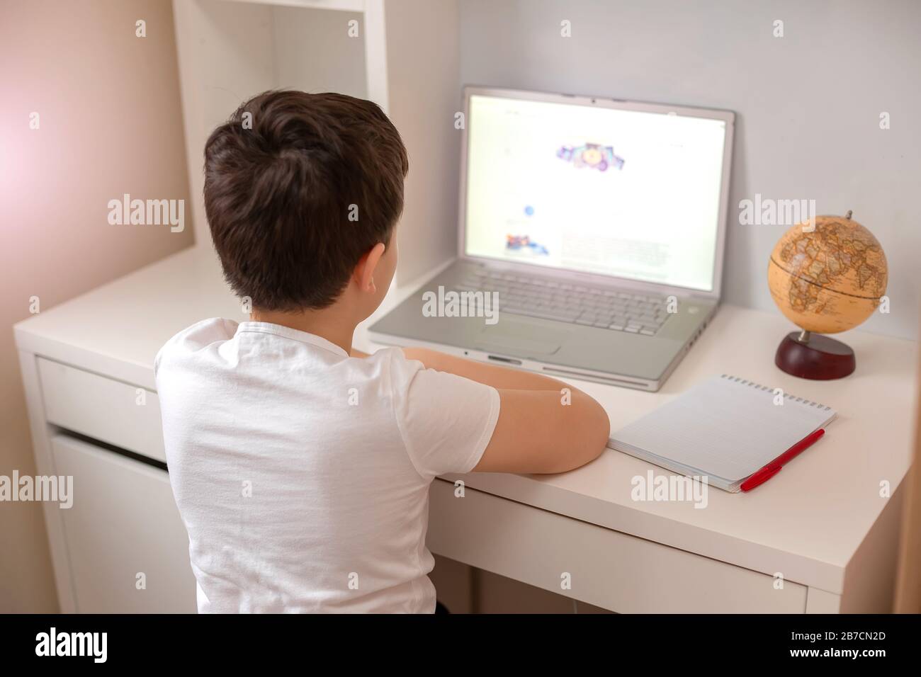 The boy sits with his back behind a laptop, looks at the monitor. Distance learning. Home Study Exam Preparation Stock Photo