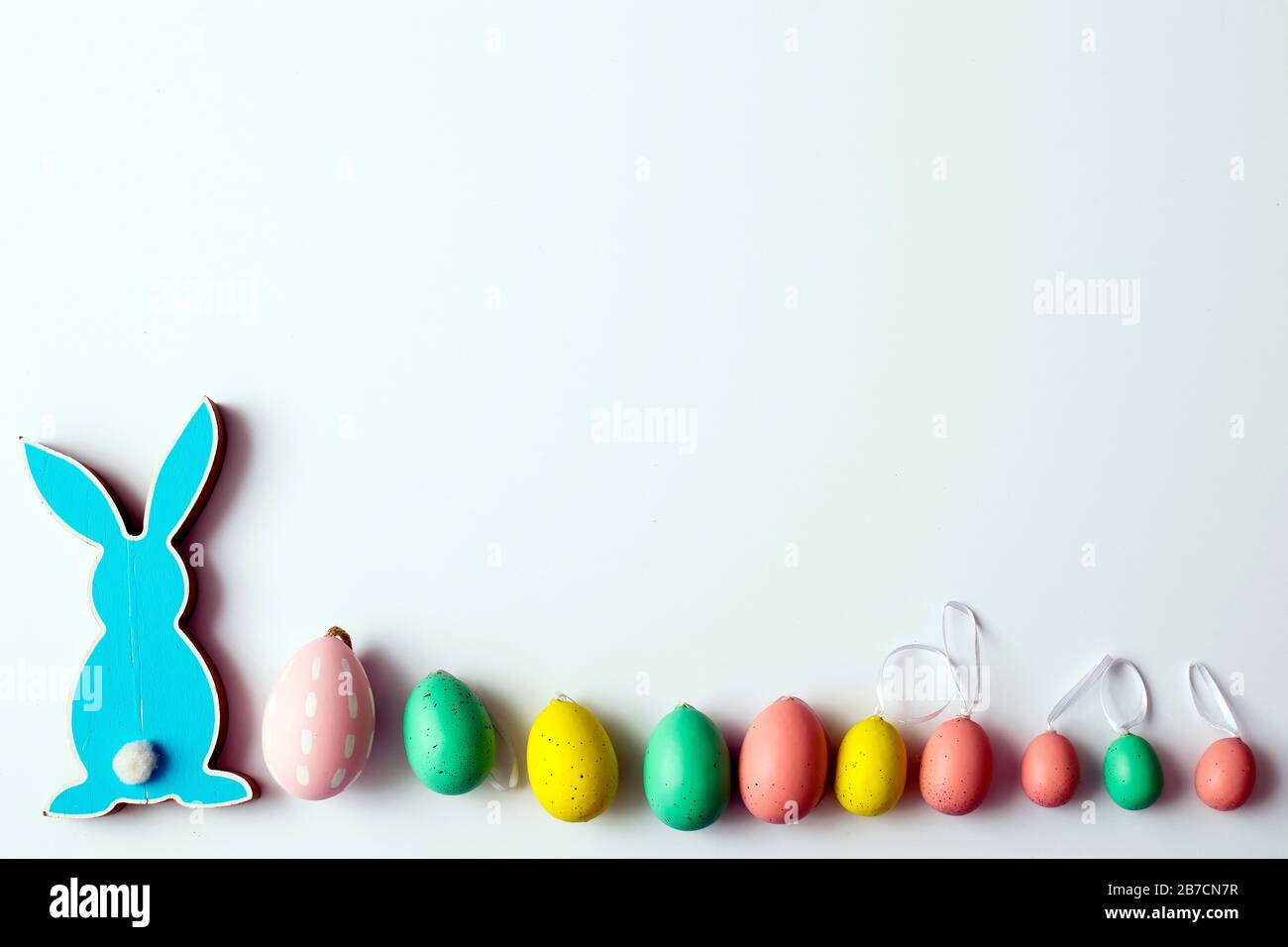 Blue wooden flat easter bunny with plastic eggs lies on a white background. Copy space Stock Photo