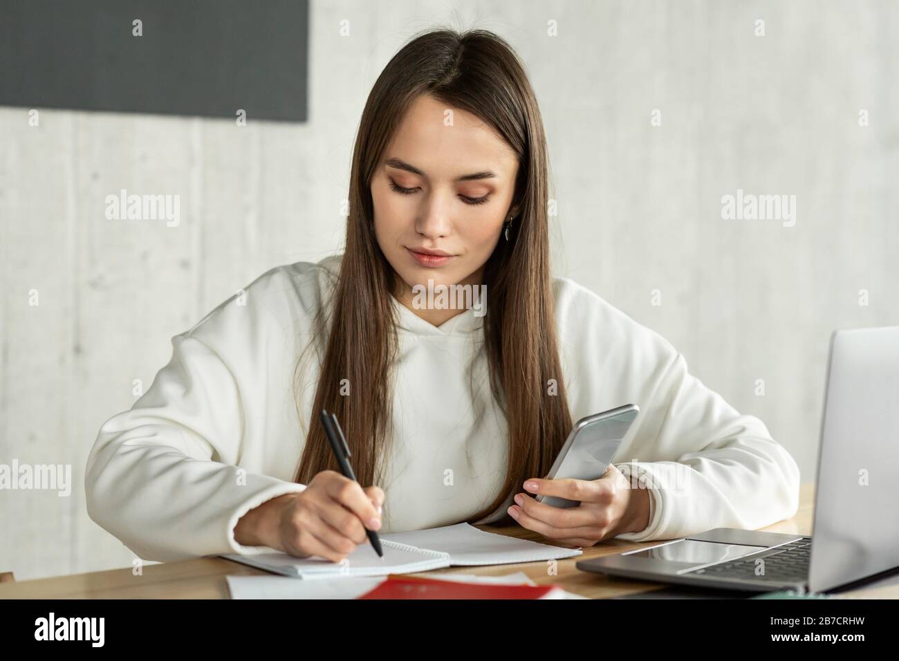Young woman freelancer makes notes at workplace Stock Photo