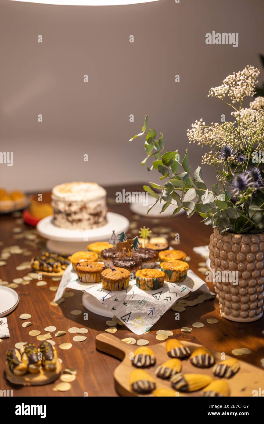 Decorated Birthday table with different cupcakes, muffins, cake and madeleines with flowers and confetti. Stock Photo