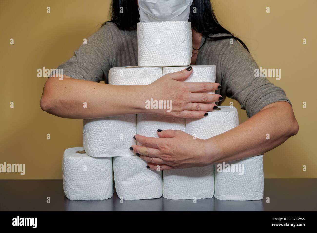 Toilet paper shortage concept with female holding rolls. Woman covers with her hands a pile of white rolls to illustrate the issue of out of stock loo Stock Photo