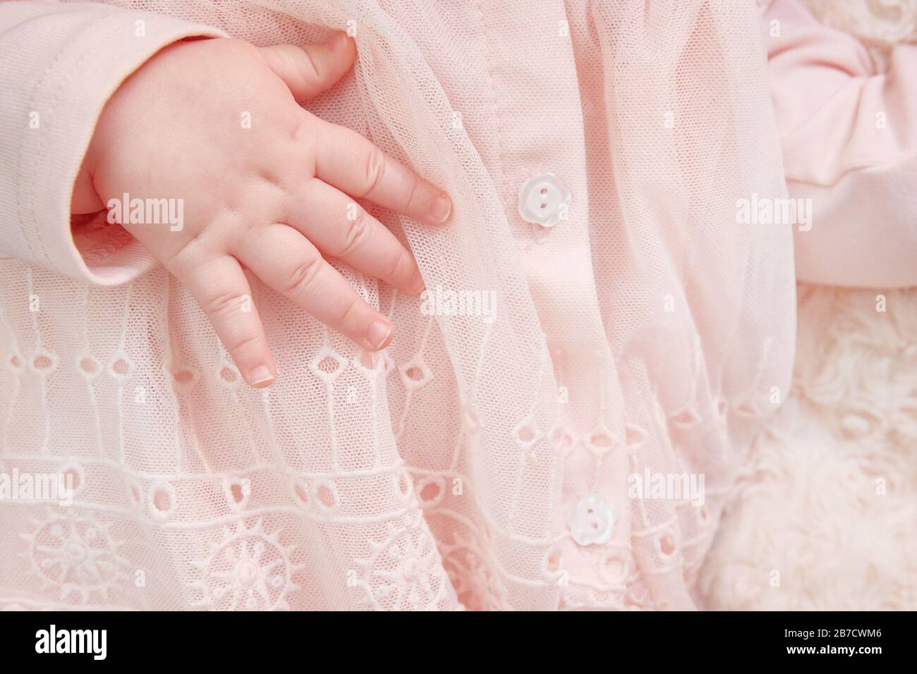 close-up of the hand of a newborn girl in a pink dress with lace and embroidery. Postcard Its a Girl. copyspace. Stock Photo